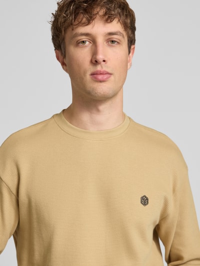 Männermodel trägt Longsleeve aus Baumwolle Modell 'FILLIP' von Blend in Beige, Label-Detail, Gerader-Schnitt, Nahaufnahme Oberkörper. Rückenlänge bei Größe M: 70 cm.