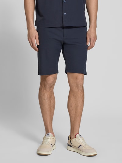Mężczyzna nosi Tapered Fit Bermuda mit Kordelzug Modell 'CHINO' od BOSS Orange, ciemnogranatowy, materiał crinkle, optyka allover-muster, przód, ujęcie całej sylwetki.