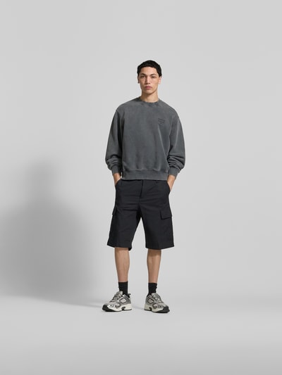 Männermodel trägt Oversized Hoodie aus Baumwoll-Mix von MAISON KITSUNÉ in Grau mit elastischen Abschlüssen im Used-Look, Ganzkörperansicht von vorne.