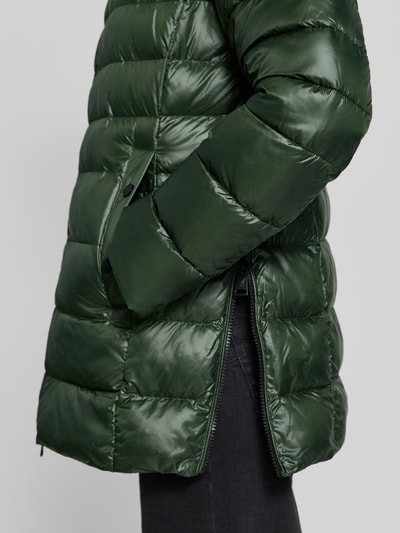 Frauenmodel trägt Regular Fit Mantel in Stepp-Optik von FUCHS SCHMITT in Dunkelgrün mit glänzender Oberfläche, Detailaufnahme, Eingrifftasche sichtbar. Kontext: Kapuze mit Tunnelzug, gefütterter Stehkragen, Zweiwege-Reißverschluss, Rückenlänge 76 cm, Schulterbreite 46 cm, Brustweite 50 cm, Ärmellänge 66 cm.