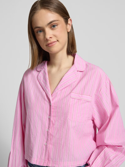Frauenmodel trägt Relaxed Fit Pyjama-Oberteil mit Brusttasche von Gina Tricot in Rosa mit weißen Streifen aus reiner Baumwolle, Nahaufnahme Oberkörper.