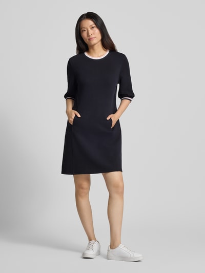 Kobiece model prezentuje Regular Fit Kleid aus Baumwoll-Mix od Marc Cain, czarna mieszanka bawełny, okrągły dekolt, długość do kolan, rękaw o dł. 1/2, długość tyłu w rozmiarze 36: 92 cm, szerokość w rozmiarze 36: 46 cm, długość rękawów w rozmiarze 36: 39 cm, gładka tekstura, widok całej sylwetki z przodu.
