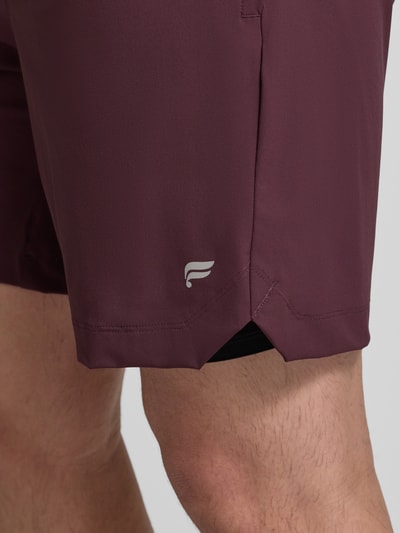 Männermodel trägt Regular Fit Shorts mit Logo-Print von Fabletics in dunklem Rot, elastischer Bund, Detailaufnahme Bein, elastischer Material-Mix.