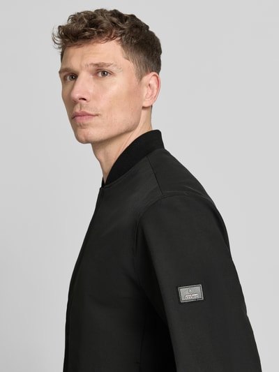 Männermodel trägt Bomberjacke mit Stehkragen Modell 'BLAASPEN' von Jack & Jones Premium, schwarz, materialmix met stretch, nahaufnahme oberkörper