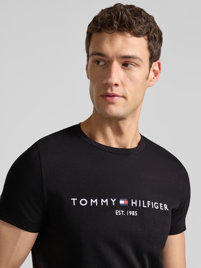 Männermodel trägt T-Shirt aus Bio-Baumwolle von Tommy Hilfiger in Schwarz mit Logo-Stickerei, gerader Schnitt, Nahaufnahme Oberkörper.
