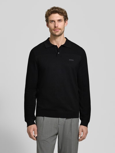 Männermodel trägt schwarzes Relaxed Fit Poloshirt mit Woll-Anteil Modell 'KN_Momentum-X PL' von BOSS Green vor grauem Hintergrund, Ganzkörperansicht von vorne.