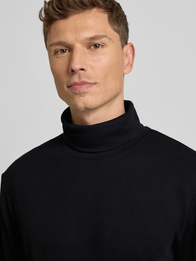 Męski model nosi Regular Fit Rollkragenpullover aus Baumwoll-Mix od Tom Tailor, jednolity, logo z przodu, z długim rękawem, bawełniany, zbliżenie na górną część ciała.