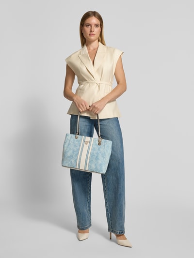 Kobiecy model nosi jasnoniebieską Tote Bag aus reiner Baumwolle Modell 'Noelle' od GUESS, tkanina stylizowana na denim, detal z logo, szerokość w rozmiarze 1: 26 cm, długość w rozmiarze 1: 37 cm, głębokość w rozmiarze 1: 10 cm, długość paska na ramię w rozmiarze 1: 60 cm, główna przegroda z zamkiem błyskawicznym, torba na ramię, widok całej sylwetki z przodu.