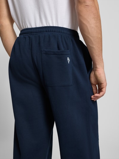 Męski model nosi granatowe spodnie Sweathose mit Biese und Varsiety Embleme od REVIEW, bawełna ze stretchem, kieszeń z tyłu, widok z tyłu.