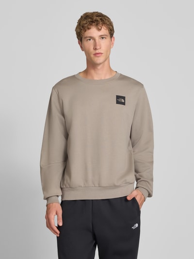 Männermodel trägt Regular Fit Sweatshirt mit Logo-Detail von The North Face in beige aus katoenmix, ronde hals, elastische boordjes, ruglengte maat M 60 cm, mouwlengte maat M 70 cm, logodetail links op de borst. Ganzkörperansicht von vorne.