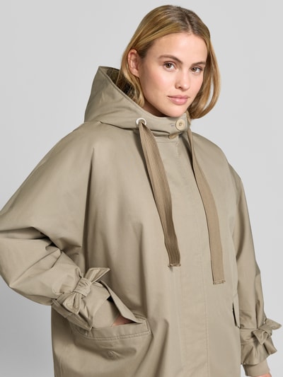 Vrouwenmodel draagt Relaxed Fit lange jas van katoenmix Model 'Livia' van g-lab in beige, met capuchon en elastische mouwboorden, Nahaufnahme Oberkörper. Ruglengte maat S 109 cm, schouderbreedte 53 cm, borstwijdte 72 cm, mouwlengte 55 cm.
