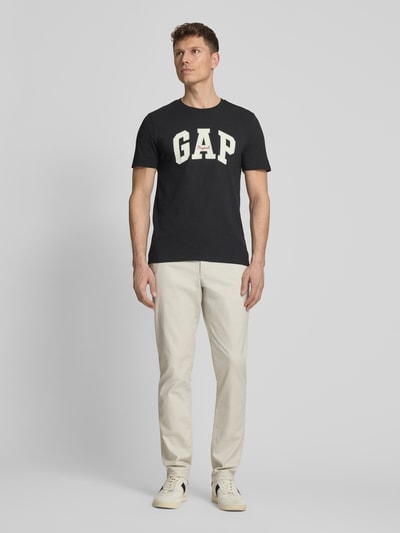 Männermodel trägt schwarzes T-Shirt mit Logo und Rundhalsausschnitt von GAP aus Reine Baumwolle, Regular-Fit, Rückenlänge 69 cm, Ganzkörperansicht von vorne.