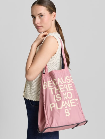Frauenmodel trägt Shopper mit Statement-Print Modell 'PACHO' von ECOALF in Rosa, weiße Schrift, offenes Hauptfach, Tragehenkel, Nahaufnahme Oberkörper.