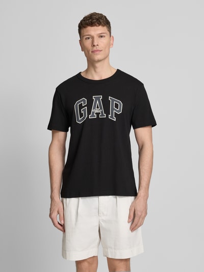 Männermodel trägt T-Shirt mit Logo und Rundhalsausschnitt von GAP, schwarze Farbe, Reine Baumwolle, Regular-Fit, Ganzkörperansicht von vorne. Rückenlänge bei Größe M: 66 cm.
