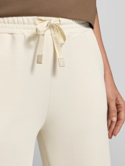 Kobiece model nosi Wide Fit Sweatpants in verkürzter Passform Modell 'Banu' od Soyaconcept, elastyczna mieszanka materiałów z domieszką modalu, jasny kolor, widoczny elastyczny pas z tunelowym wiązaniem, spodnie dresowe, detaliczny widok z przodu, zbliżenie na górną część nóg.