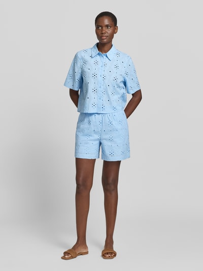 Frauenmodel trägt Regular Fit Shorts aus reiner Baumwolle Modell 'ELIZA' von Vero Moda in hellblauer Unifarbe mit Lochstickerei, Ganzkörperansicht von vorne.