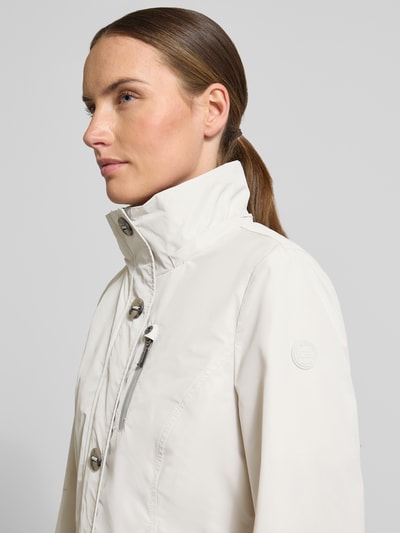 Vrouwenmodel draagt Jacke mit Kapuze und Eingrifftaschen van Gil Bret in licht beige met ritszakken, regular fit, knoopsluiting, weer protection, ruglengte maat 36: 67 cm, schouderbreedte: 40 cm, borstwijdte: 46 cm, mouwlengte: 64 cm. Nahaufnahme bovenlichaam.