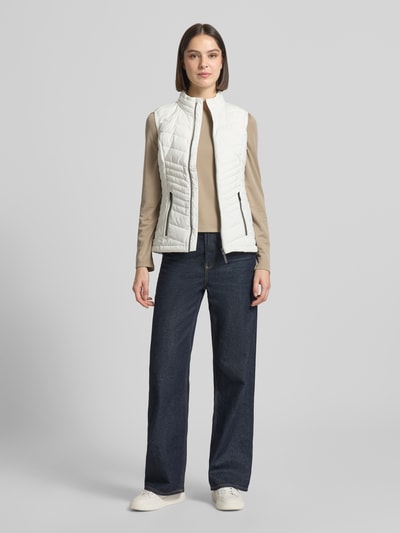 Vrouwenmodel draagt witte bodywarmer met opstaande kraag, ritssluiting, ritszakken, slim fit, model 'GS109' van G.I.G.A. DX, ruglengte maat 36: 61 cm, schouderbreedte: 37 cm, borstwijdte: 49 cm, 10.000 mm waterkolom. Ganzlichaansicht van voren.
