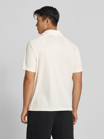 Männermodel trägt Relaxed Fit Poloshirt mit Logo-Stitching von Champion in Creme, glatte Textur, kurzer Ärmel, Ganzkörperansicht Rückansicht. Herren Poloshirt von Champion, Polokragen, Rückenlänge bei Größe M 70 cm.