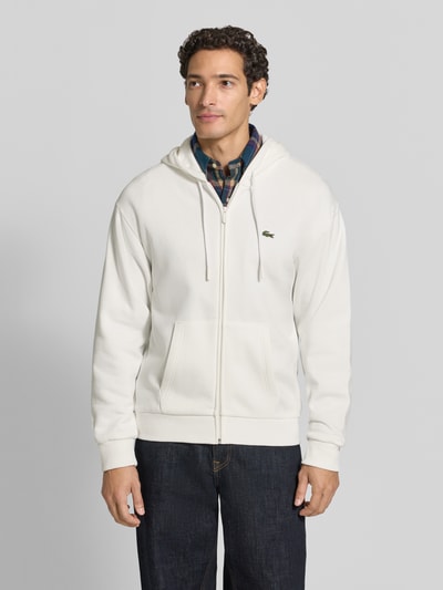 Männermodel trägt Regular Fit Sweatjacke aus Baumwoll-Mix von Lacoste in Weiß, glatte Textur, Ganzkörperansicht von vorne, Herren Sweatjacke von Lacoste.