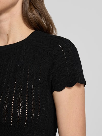 Frauenmodel trägt Slim Fit Strickpullover aus Viskose-Mix Modell 'FICE' von BOSS Orange in schwarzer Strickoptik mit Struktur-Muster, Label-Applikation, Rundhals-Ausschnitt und Kurzarm, Nahaufnahme Oberkörper.