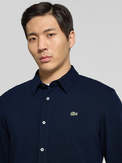 Männermodel trägt Slim Fit Freizeithemd aus reiner Baumwolle von Lacoste in Dunkelblau, Optik: Unifarben, Logo-Stitching, Nahaufnahme Oberkörper.