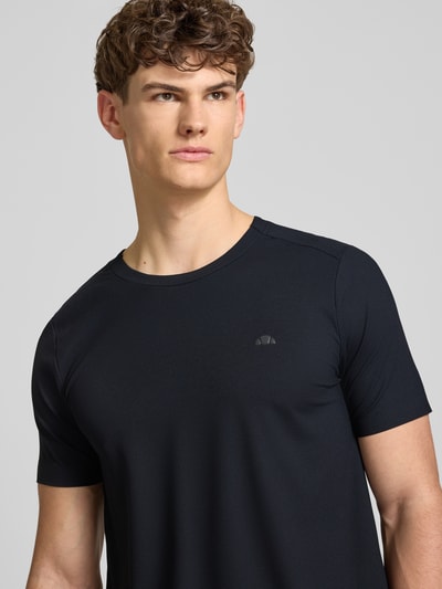 Männermodel trägt T-Shirt mit Strukturmuster Modell 'TELLER TEE' von Ellesse in Schwarz, Logo auf der Brust, Nahaufnahme Oberkörper. Material-Mix, Regular Fit.