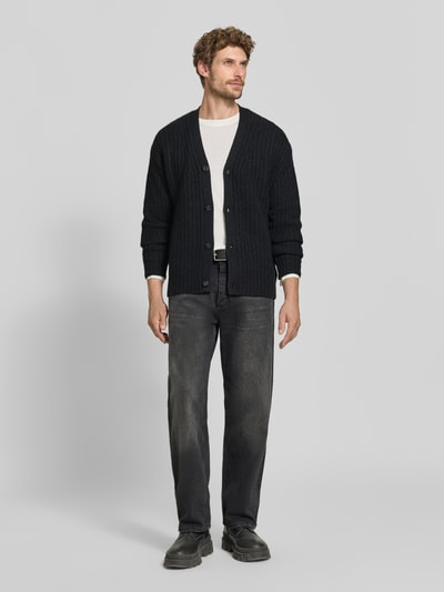 Männermodel trägt Cardigan aus Kaschmir-Mix mit V-Ausschnitt von FTC Cashmere in Schwarz mit Knopfleiste, geradem Schnitt, Ganzkörperansicht von vorne.