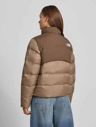 Frauenmodel trägt Steppjacke mit Reißverschlusstaschen Modell 'SAIKURU' von The North Face, krój regular fit, stójka, wyhaftowane logo, zamek błyskawiczny, beżowo-brązowe bloki kolorystyczne, gładka tekstura, długość tyłu w rozmiarze S: 59 cm, szerokość ramion w rozmiarze S: 43 cm, szerokość w rozmiarze S: 53 cm, długość rękawów w rozmiarze S: 62 cm, Ganzkörperansicht Rückansicht