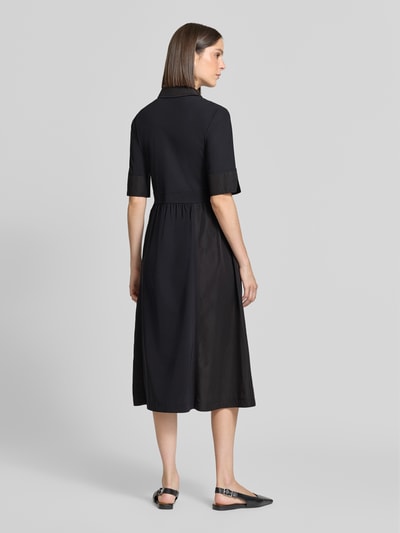 Vrouwenmodel draagt Midikleid met Umlegekragen van Marc Cain, in zwart, elastische materiaalmix, getailleerde pasvorm, steekzakken, ruglengte maat 36: 120 cm, borstwijdte 46 cm, mouwlengte 32 cm, halve mouwen, platte kraag, doorlopende knoopsluiting, geheel achteraanzicht.
