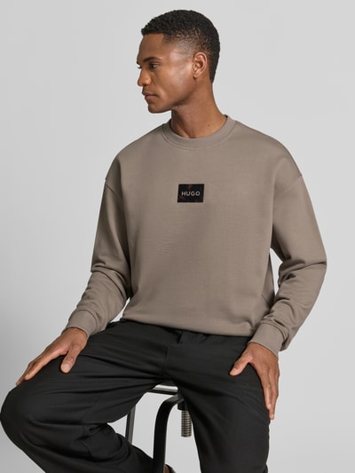 Männermodel trägt Regular Fit Sweatshirt aus reiner Baumwolle Modell 'DAYLO' von HUGO, Optik: Unifarben, Label-Applikation, Rundhals, Langarm, Ärmelabschluss und Rumpfabschluss gerippt, Materialverarbeitung: Sweat, Farbe taupe, glatte Struktur, Nahaufnahme Oberkörper.