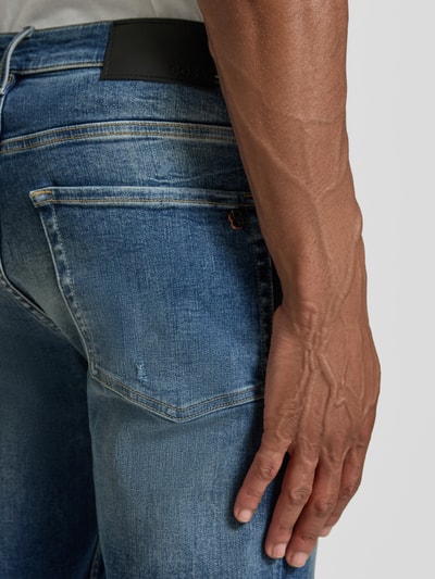 Mannenmodel draagt Slim Fit Jeans aus Baumwoll-Mix Modell 'ONYX' van BOSS Orange in blauwe tinten, detailopname achterkant.