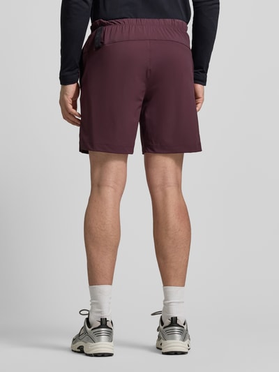 Männermodel trägt Regular Fit Shorts mit Logo-Print von Fabletics, bordeauxrot, elastischer Bund, Ganzkörperansicht Rückansicht.