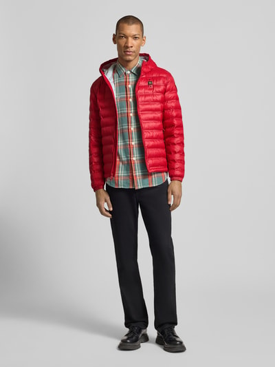 Männermodel trägt rote Steppjacke mit Zweiwege-Reißverschluss Modell 'Charles' von Blauer Usa, Regular Fit, Kapuze, Label-Detail, Ganzkörperansicht von vorne.
