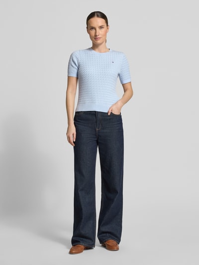 Vrouwenmodel draagt Slim Fit T-shirt uit puur katoen van Tommy Hilfiger in look: effen kleuren met kabelpatroon, logodetail, ronde hals, korte mouw, knitwear, kleur lichtblauw, geribde zoom, geheel vooraanzicht.