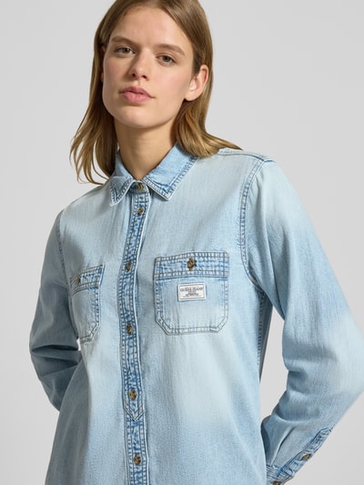 Frauenmodel trägt Regular Fit Jeansbluse mit Brusttaschen und Label-Detail von Guess aus reiner Baumwolle, Nahaufnahme Oberkörper.