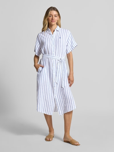 Modelka kobieca ma na sobie Oversized Hemdblusenkleid aus reinem Leinen od Lauren Ralph Lauren, białe i niebieskie paski, lniany materiał, długość midi, krótki rękaw, kołnierzyk koszulowy, zapięcie na guziki, pasek, logo, krój oversize, flammgarn, widok całej sylwetki z przodu