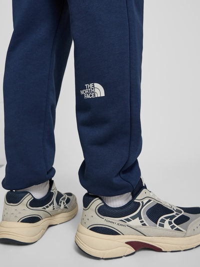 Männermodel trägt Sweatpants mit Logo-Print von The North Face in Dunkelblau, Baumwoll-Mix, elastischer Bund, Detailaufnahme Beine