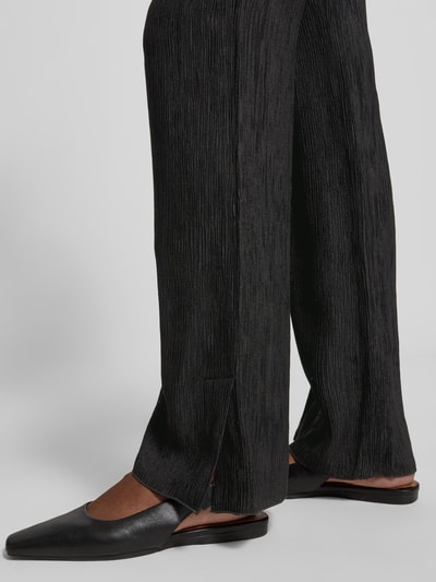 Frauenmodel trägt Straight Fit Stoffhose aus Viskose-Mix von Anine Bing mit Strukturmuster, Elastikbund und Eingrifftaschen, Nahaufnahme Unterbein.