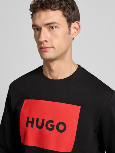 Männermodel trägt Sweatshirt mit Label-Print Modell 'Duragol' von HUGO aus reiner Baumwolle, schwarzer Stoff, Nahaufnahme Oberkörper.