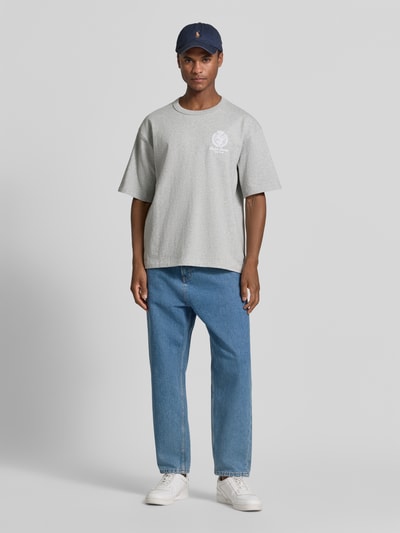 Mannenmodel draagt Relaxed Fit T-shirt uit pure katoen van Polo Ralph Lauren in lichtgrijs met blauwe jeans en witte sneakers. Volledige vooraanzicht.