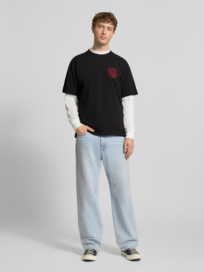 Männermodel trägt Herren T-Shirt aus Reiner Baumwolle Modell 'MUSIC CHANNEL' von Edwin, schwarze Töne, Gerader-Schnitt, Ganzkörperansicht von vorne. Rückenlänge bei Größe M: 70 cm, Rundhalsausschnitt.