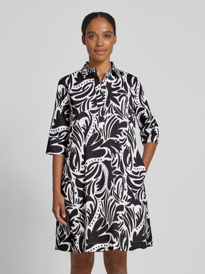 Frauenmodel trägt Knielanges Hemdblusenkleid mit verdeckter Knopfleiste von Christian Berg Woman in Schwarz-Weiß mit floralem Muster, Reine Baumwolle, Straight Fit, Hemdblusenkragen, 1/2-Arm, Knielänge, Brustweite 54 cm, Rückenlänge 95 cm, Ärmellänge 40 cm, Nahaufnahme Oberkörper.