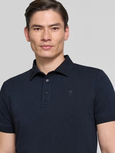 Męski model nosi Regular Fit Poloshirt mit Knopfleiste Modell 'Carlosjuan' von JOOP! Collection, bawełniany miks ze stretchem, krój regular fit, ciemnogranatowy kolor, kołnierzyk polo, krótka listwa guzikowa, długość pleców w rozmiarze M: 69 cm, zbliżenie na górną część ciała.