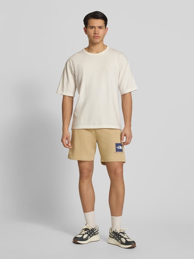 Męski model nosi Regular Fit Shorts mit Eingrifftaschen von The North Face z mieszanki bawełny, beżowy kolor, wpuszczane kieszenie, kieszeń z tyłu, szerokość w rozmiarze M: 40 cm, długość wewnętrzna nogawki: 18 cm, Ganzkörperansicht von vorne.