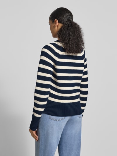 Frauenmodel trägt Regular Fit Strickpullover aus reiner Baumwolle von Tommy Hilfiger, Optik:Allover-Muster, gestreift, Zierknöpfe, Logo-Applikation aus Metall, Crew Neck, Langarm mit Raglanärmel, gerippte Abschlüsse, Materialverarbeitung: Strick, Ganzkörperansicht Rückansicht.