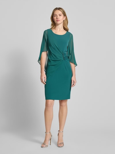 Modelka nosi Knielanges Cocktailkleid mit Rundhalsausschnitt von Vera Mont, elastyczna mieszanka materiałów, dopasowany krój, okrągły dekolt, kopertowy styl, ozdobna aplikacja z obszyciem z kamieni stras, długość do kolan, wszyty zamek błyskawiczny z tyłu, rękawy nietoperzowe z szyfonu, długość tyłu w rozmiarze 36: 98 cm, szerokość w rozmiarze 36: 108 cm, długość rękawów w rozmiarze 36: 48 cm, widok całej sylwetki z przodu.
