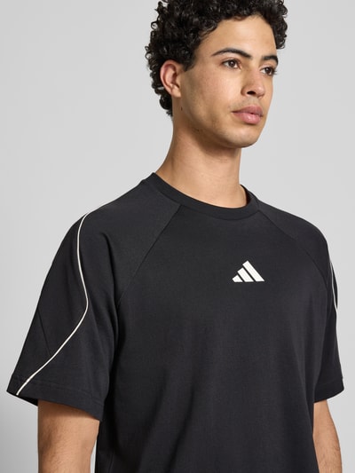 Männermodel trägt T-Shirt mit Label-Print von adidas Sportswear in Schwarz, reine Baumwolle, Regular-Fit, gerippter Rundhalsausschnitt, Nahaufnahme Oberkörper.