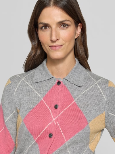 Frauenmodel trägt Regular Fit kardigan rozpinany z dodatkiem wełny od Jake*s Casual, wzór na całej powierzchni w szkocką kratę, zapięcie na listwę guzikową, kołnierzyk polo, długi rękaw, dzianina, detal z logo, prążkowane zakończenia, widoczny szary, różowy i beżowy kolor, wykończenie z dzianiny, Ganzkörperansicht von vorne