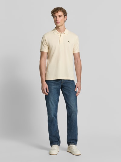 Männermodel trägt Regular Fit Poloshirt aus reiner Baumwolle von Lacoste in Creme, kombiniert mit blauen Jeans, Ganzkörperansicht von vorne, Herren Poloshirt von Lacoste